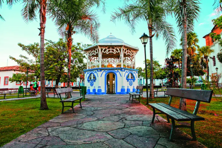 Coreto histórico pintado de azul e branco no centro da Cidade de Goiás, com bancos e palmeiras ao redor, em ambiente ensolarado.