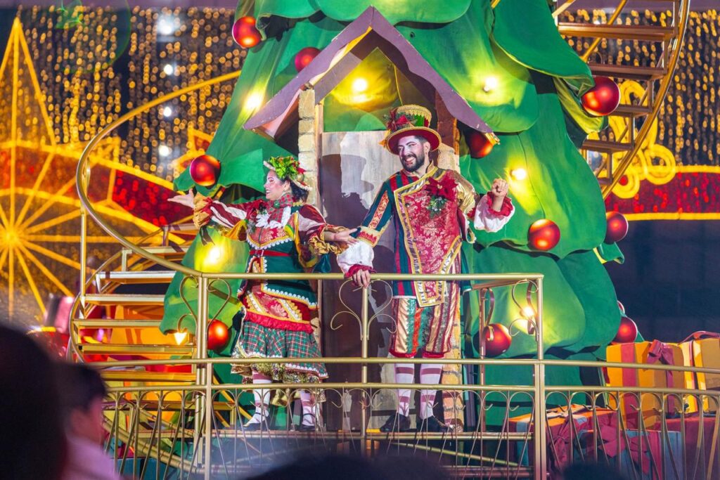 Artistas se apresentam na Árvore de Natal cenográfica, ocupando diferentes níveis da estrutura em um espetáculo coreografado.