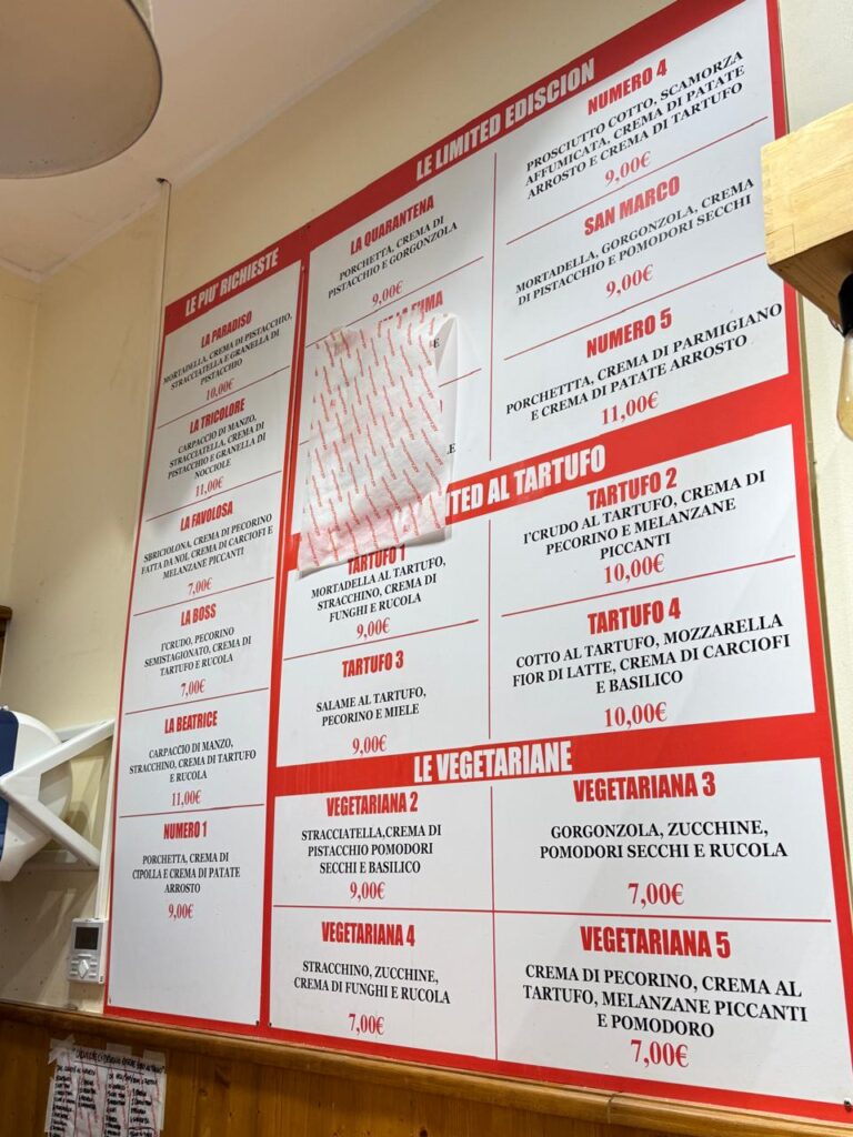 Cardápio vermelho e branco do All’Antico Vinaio em Roma, exibindo os nomes dos sanduíches mais pedidos.