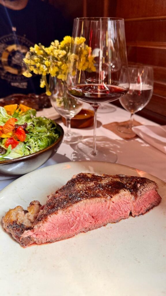 Corte de Entrecot com o ponto perfeito, acompanhado de salada e um bom vinho.