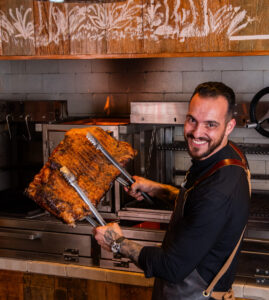 Pedro Nunes em frente à parrilla do Asador Nunes segurando uma costela assada durante o lançamento do projeto O Fogo Nos Une, em São Paulo.