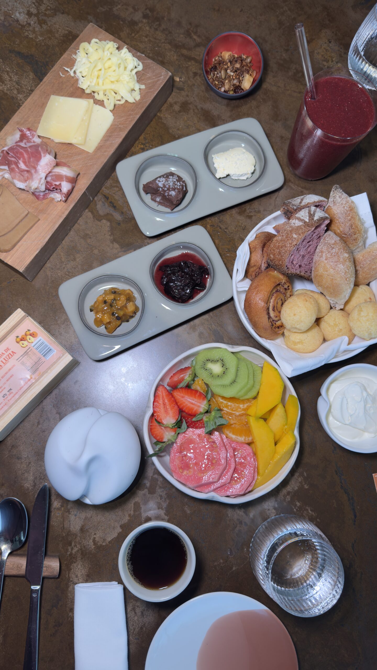 Mesa de café da manhã do Íz Hotel Conceito, em Goiânia, com seleção de frutas frescas, pães artesanais, queijos, charcutaria, pães de queijo, compotas e acompanhamentos servidos à la carte.