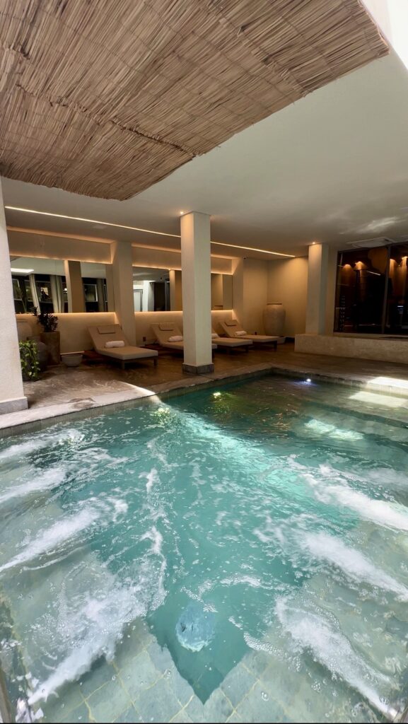 Área de bem-estar do Íz Hotel Conceito, em Goiânia, com piscina aquecida, hidromassagem, espreguiçadeiras e ambiente interno dedicado ao relaxamento dos hóspedes.