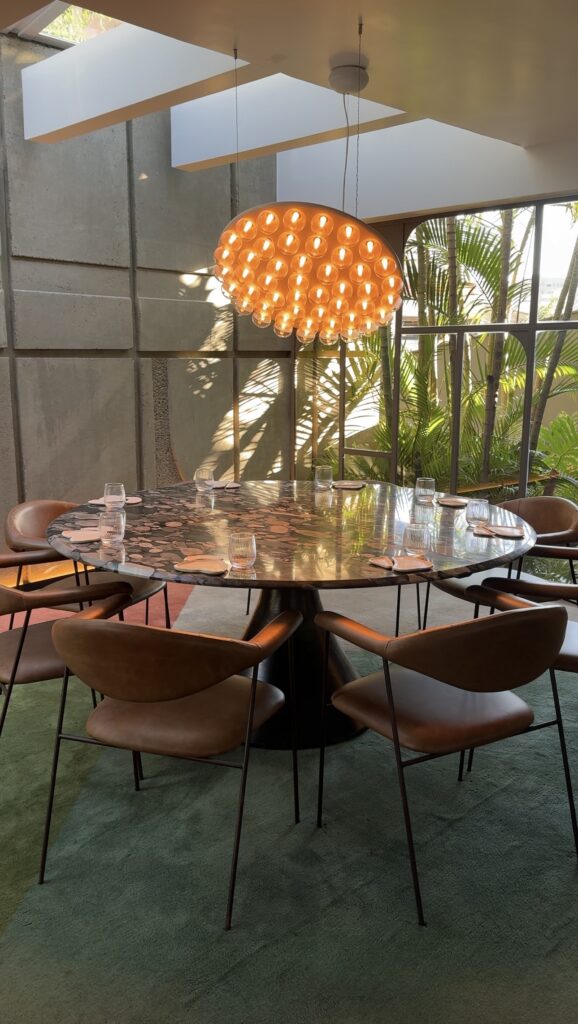 Ambiente interno do restaurante Íz, no Íz Hotel Conceito, em Goiânia, com mesa redonda, luminária contemporânea, jardim interno e arquitetura moderna.
